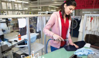 Eine Frau reinigt in einer Wäscherei ein Textilstück.