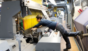 Ein Mann beugt sich über eine Textilmaschine und prüft das Arbeitsstück.