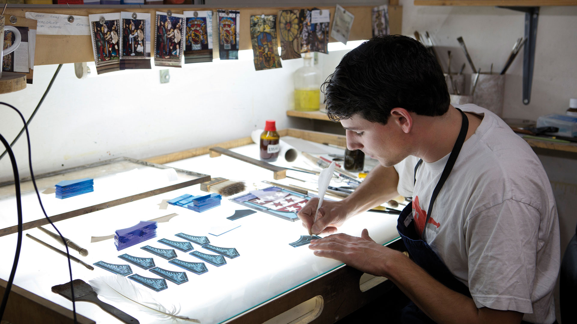 Ein Mann bemalt in einem Atelier Glasstücke.