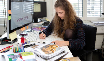 Eine Frau erstellt in einer Büroumgebung eine Skizze in ihrem Skizzenbuch.