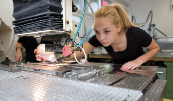 Eine Frau benutzt eine Maschine um ein Objekt zu gravieren.
