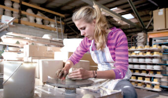 Eine Frau formt mithilfe einer Töpferscheibe einen Gegenstand.