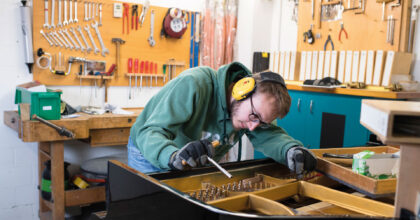 Ein Mann stimmt das Klavier, indem er die Saiten anzieht.