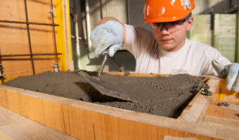 Auf einer Baustelle füllt ein Mann Beton in eine Holzschalung.