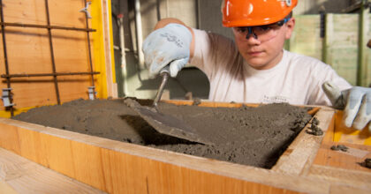 Auf einer Baustelle füllt ein Mann Beton in eine Holzschalung.