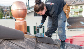 Eine Frau montiert Dachziegel auf dem Dach eines Hauses.