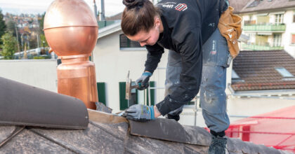 Eine Frau montiert Dachziegel auf dem Dach eines Hauses.