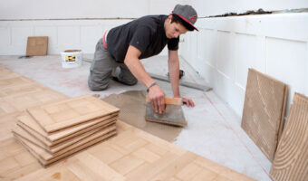 Ein Mann verlegt in einem Haus Parkettboden.