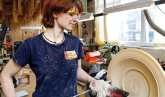 Eine Frau drechselt in einem Atelier ein rundes Holzstück.