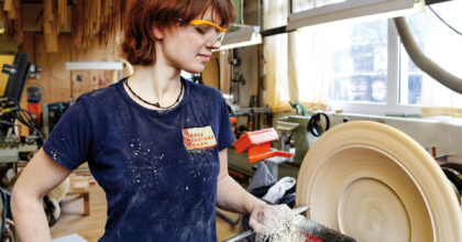 Eine Frau drechselt in einem Atelier ein rundes Holzstück.