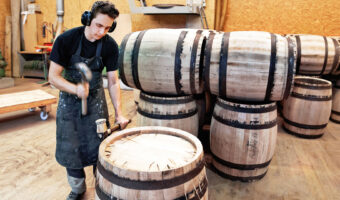 Ein Mann montiert mit einem Setzhammer Metallbügel an einem Holzfass.
