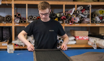 In einem Atelier bereitet ein Mann am Ende einer langen Stoffbahn einen Umschlagsaum vor.