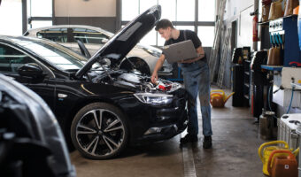 Ein Mann führt in einer Autowerkstatt mithilfe eines Laptops Wartungsarbeiten an einem Fahrzeug durch.