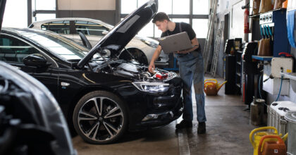 Ein Mann führt in einer Autowerkstatt mithilfe eines Laptops Wartungsarbeiten an einem Fahrzeug durch.