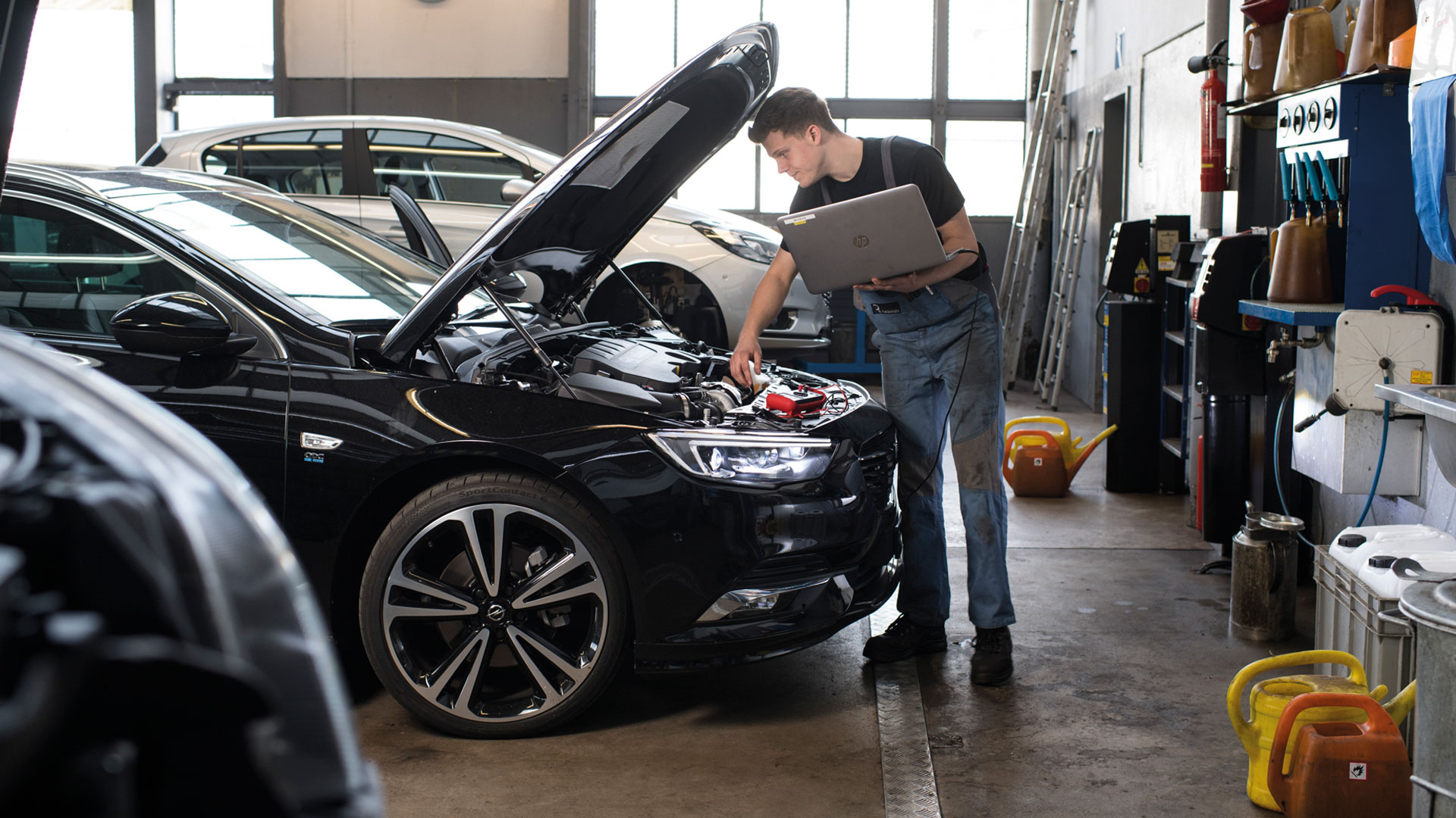 Ein Mann führt in einer Autowerkstatt mithilfe eines Laptops Wartungsarbeiten an einem Fahrzeug durch.