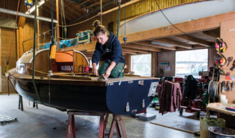 Eine Frau kniet auf einem kleinen hängenden Boot und befestigt im hinteren Teil des Bootes ein Seil.