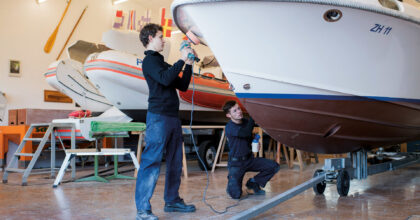 Zwei Männer polieren in einer Werkhalle ein Boot.