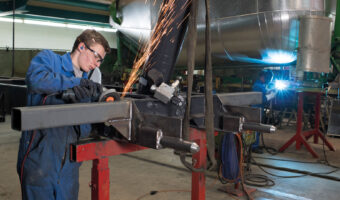 Ein Mann schleift ein quadratisches Stahlrohr.