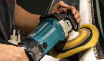 Ein Mann poliert mit einer Poliermaschine eine Autocarrosserie.