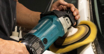 Ein Mann poliert mit einer Poliermaschine eine Autocarrosserie.