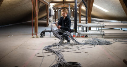 Ein Mann stellt in einem Dachstock eines Gebäudes mehrere Kabelstränge zusammen.