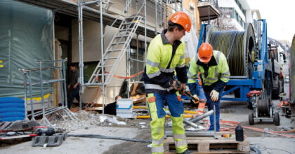 Zwei Männer montieren auf einer Baustelle ein Netzkabel.
