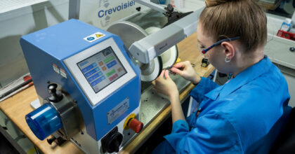 Eine Frau poliert mit einer Maschine ein Uhrenteil.