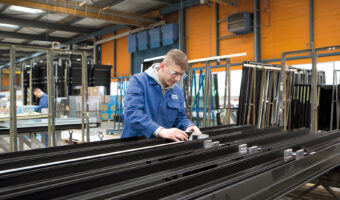 Ein Mann misst in einer Industriehalle ein Metallbauteil.