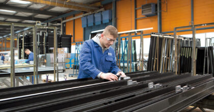 Ein Mann misst in einer Industriehalle ein Metallbauteil.