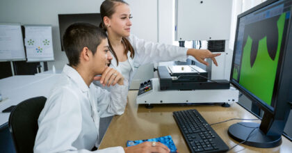 Eine Frau zeigt vor ihrem Kollegen auf einen Bildschirm auf dem Werte zu einem Zahnrad angezeigt werden.