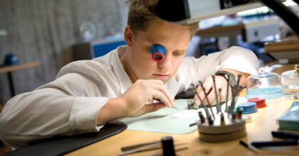 Ein Mann mit einer Monokellupe am Auge arbeitet an einem Uhrwerk.
