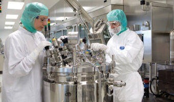 Zwei Personen in Schutzbekleidung arbeiten in einer Laborumgebung an einem Laborgerät.