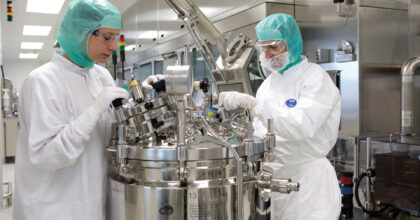 Zwei Personen in Schutzbekleidung arbeiten in einer Laborumgebung an einem Laborgerät.