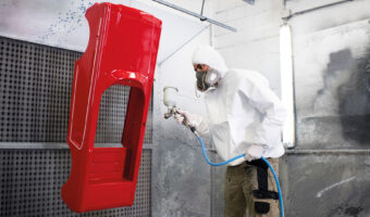 Ein Mann in Schutzkleidung beschichtet mit einer Spritzpistole ein industriell hergestelltes Produkt aus Kunststoff.