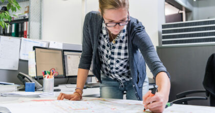 Eine Frau markiert mit einem Leuchtstift Stellen im Plan eines Gebäudes.