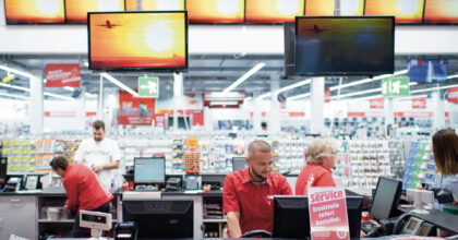 Verkaufspersonal eines Elektronikfachhandels beim Einkassieren und Beraten an der Kasse.