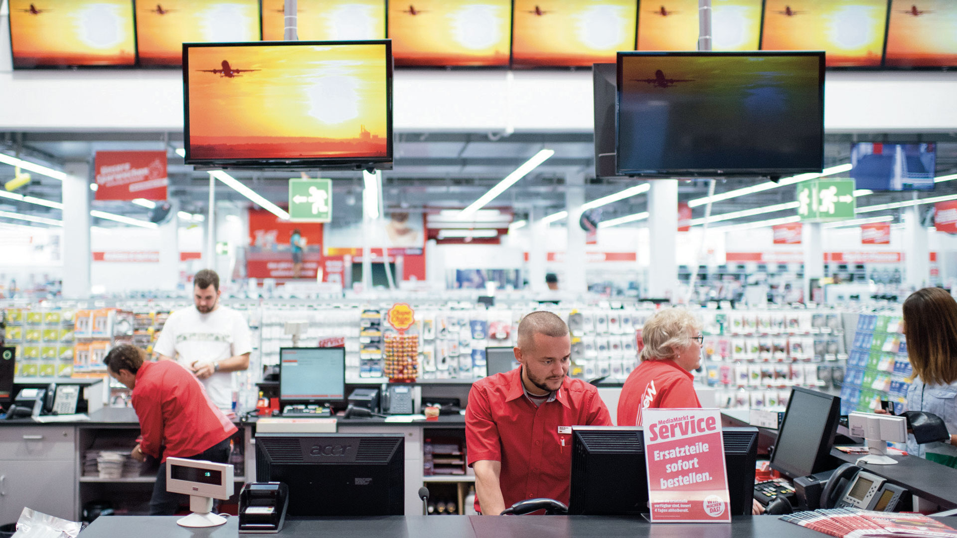 Verkaufspersonal eines Elektronikfachhandels beim Einkassieren und Beraten an der Kasse.