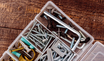 Ein Plastikkistchen mit Schrauben, Dübeln und Sechskantschlüssel liegt geöffnet auf rohen Holzbrettern.