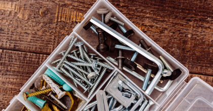 Ein Plastikkistchen mit Schrauben, Dübeln und Sechskantschlüssel liegt geöffnet auf rohen Holzbrettern.