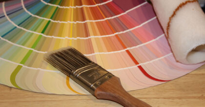 Auf einem Tisch liegen ein Farbfächer, ein dicker Pinsel und ein Farbroller.