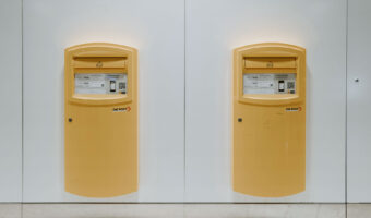 An einer weissen Wand sind zwei gelbe Postbriefkästen montiert.