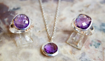 Auf einer Marmorplatte sind zwei Silberringe und eine Silberkette mit violettem Stein platziert.