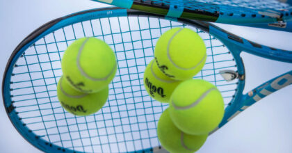 Drei neongelbe Tennisbälle liegen auf einem Spiegel in dem sich ein Tennisschläger spiegelt.