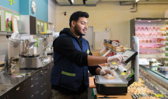 Ein Mann wägt Käse an der Käsetheke.