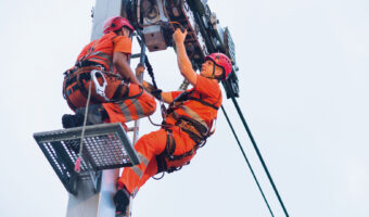 Zwei Männer führen Wartungsarbeiten an der Stütze einer Seilbahn durch.