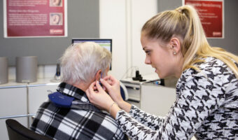 Eine Frau führt bei einem älteren Herrn einen akustischen Test durch.