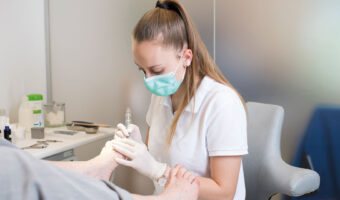 Eine Frau mit Schutzmaske führt an einer Patientin eine Fussbehandlung durch.