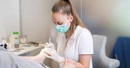 Eine Frau mit Schutzmaske führt an einer Patientin eine Fussbehandlung durch.