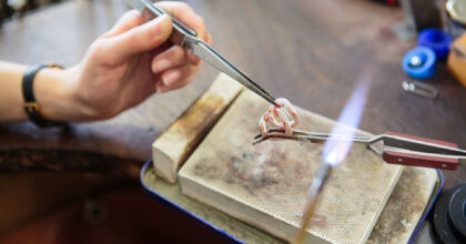 Frauenhände halten mit Pinzetten zwei glühende, miteinander verbundene Kettenglieder.