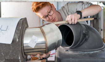 Ein Mann misst mit einem Zollstock den Abstand von einem Rohr zum Ofen.